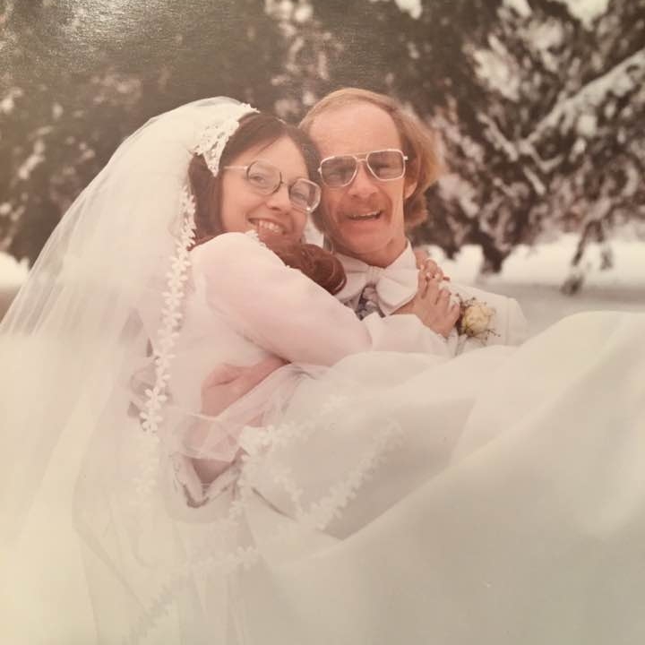 John Wright holds Judy in her gown at their wedding in 1976, with snow on the evergreen trees in the background